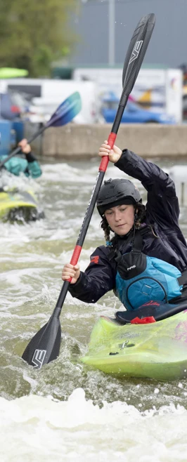 A student in a colourful kayak paddling through fast-moving water, wearing a helmet and safety gear. A student in a colourful kayak paddling through fast-moving water, wearing a helmet and safety gear.